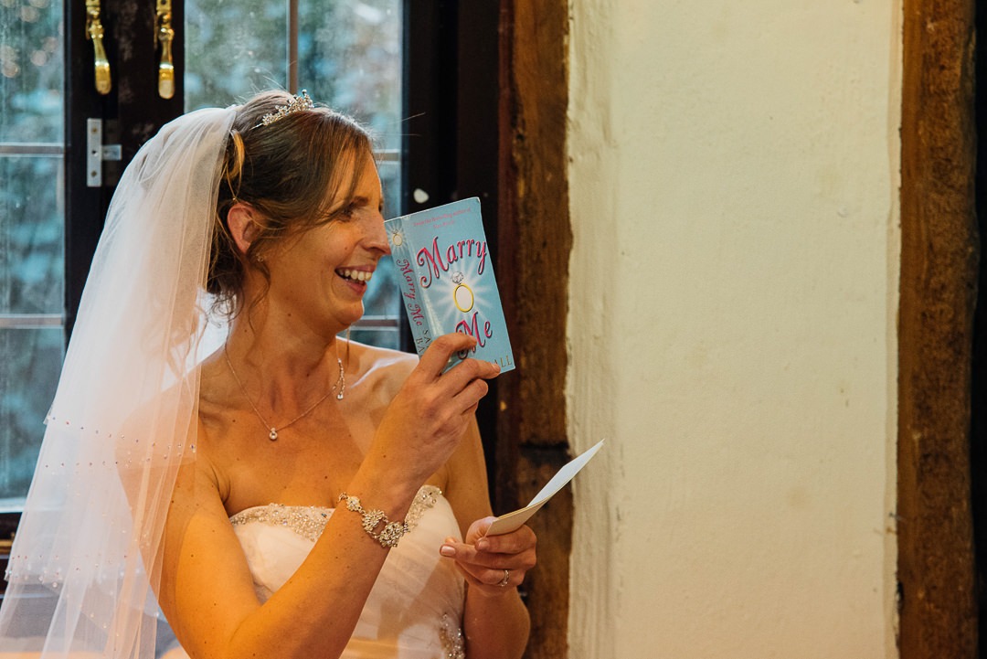 Bride holds up a book that says 'Marry Me' during a speech